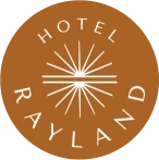This image shows a brown circular logo with “Hotel Rayland” written around a stylized sunburst design.