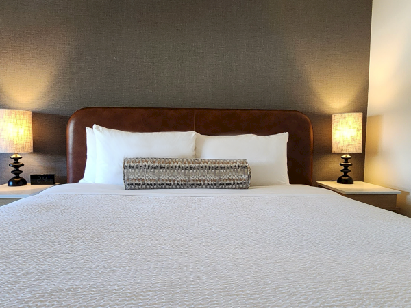 A neatly made bed with a white coverlet, flanked by two bedside tables and lamps, set against a gray wall.