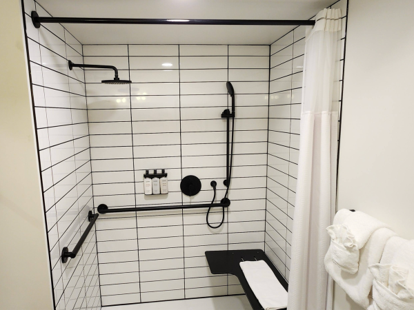 A modern shower with white subway tiles, black fixtures, a bench, and a shower curtain. Towels are neatly stacked on a bar.