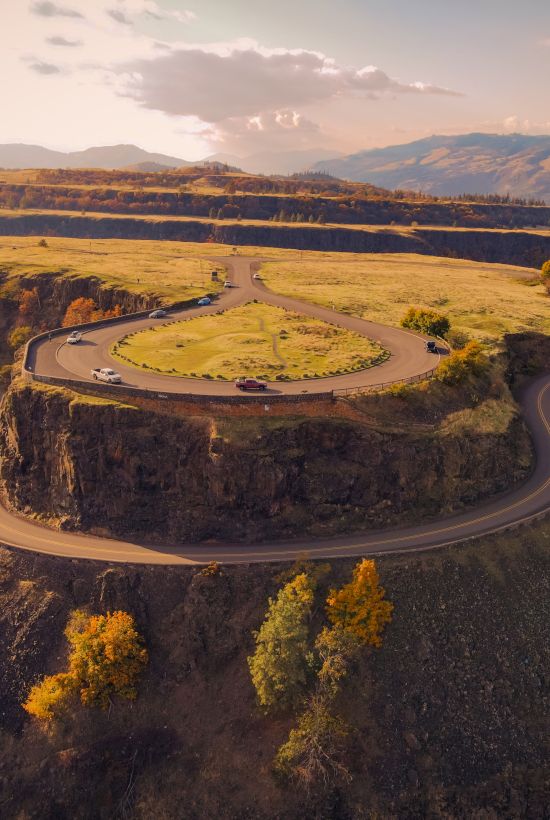 A winding road leads to a scenic overlook atop a steep, rocky hill with a circular design, surrounded by autumn trees and expansive landscape.