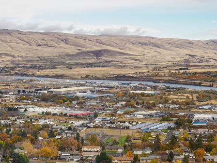 A town surrounded by autumn trees, amidst a dry, rolling hillside landscape under a partly cloudy sky, creates a serene, picturesque view.