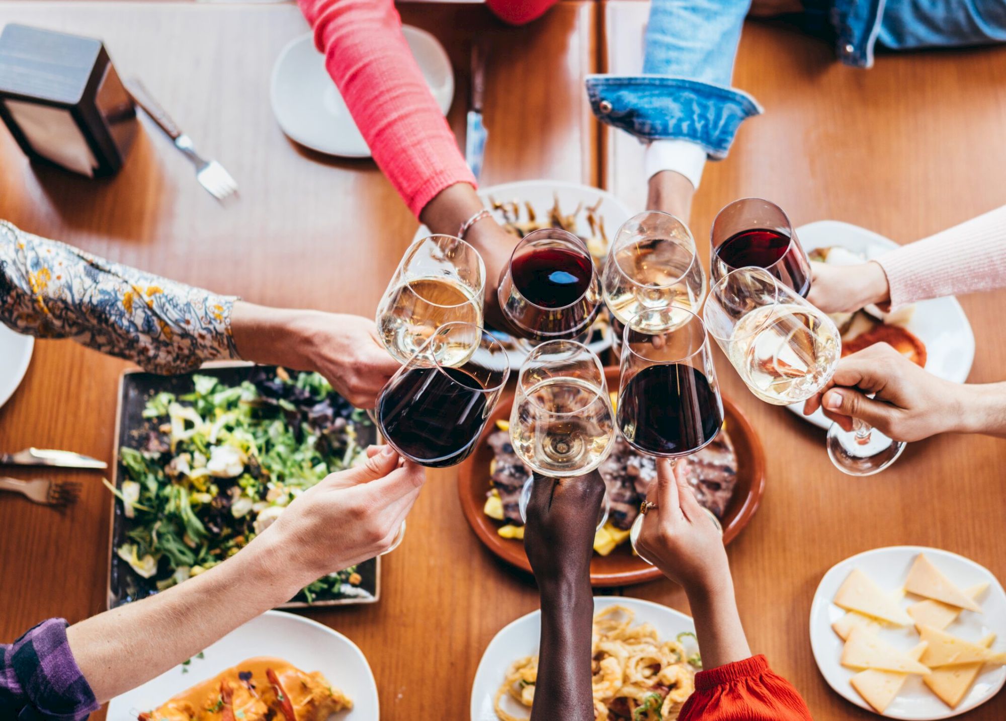 A group of people clinking glasses over a table with assorted dishes, including salad, pasta, and cheese.