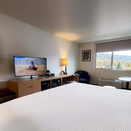 A bright hotel room with a bed, desk, wall art, and a seating area; modern and cozy with warm lighting.
