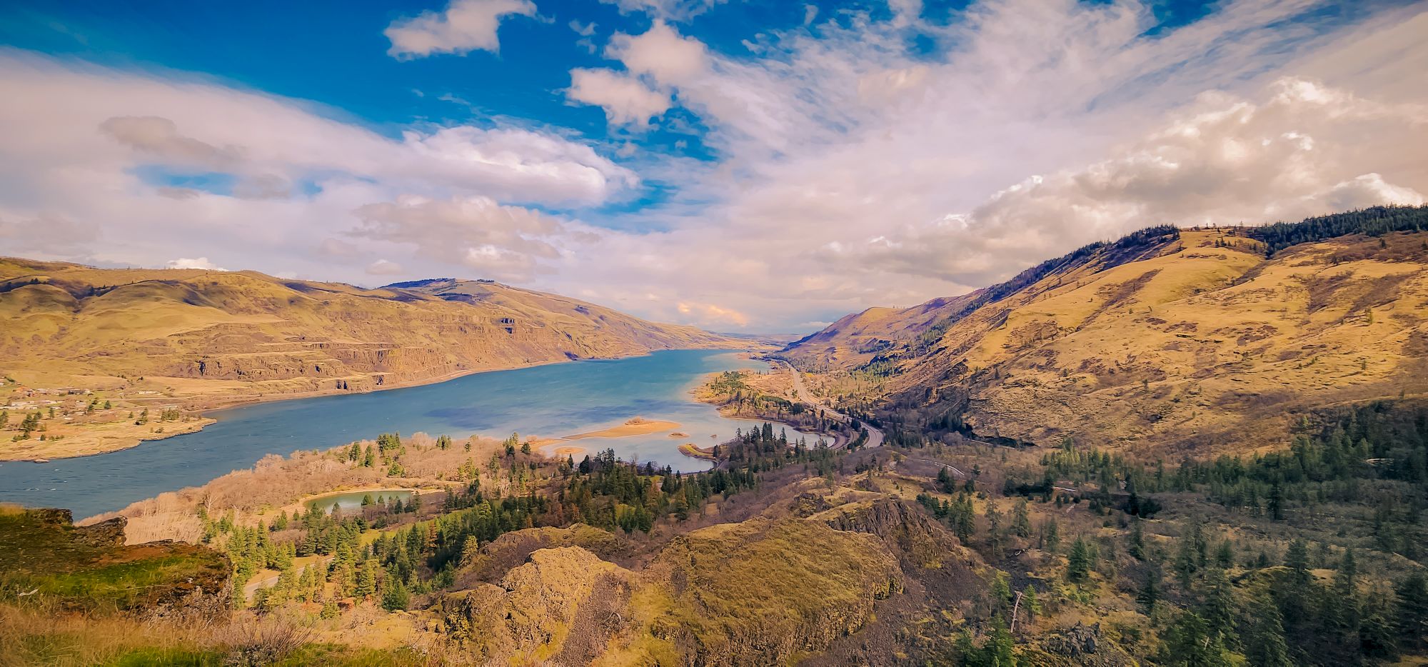 The image shows a river flowing through a rocky, mountainous landscape under a blue sky with clouds.